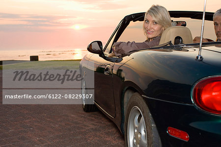 Woman sitting in convertible at sunset