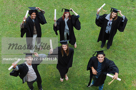 Graduates holding their degrees on grass