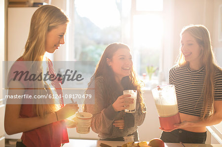 Teenage girls making smoothie in sunny kitchen