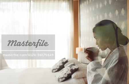 Woman in bathrobe sipping coffee in bedroom
