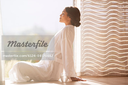 Serene woman in bathrobe sitting cross-legged at sunny doorway