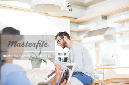 Couple drinking coffee, reading newspaper and using digital tablet in kitchen