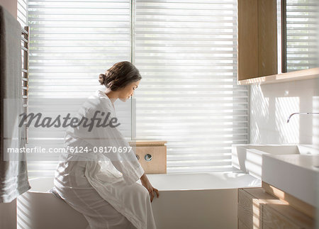 Woman in bathrobe drawing a bath in soaking tub in luxury bathroom