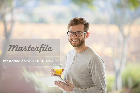 Portrait smiling man drinking orange juice and using digital tablet on patio