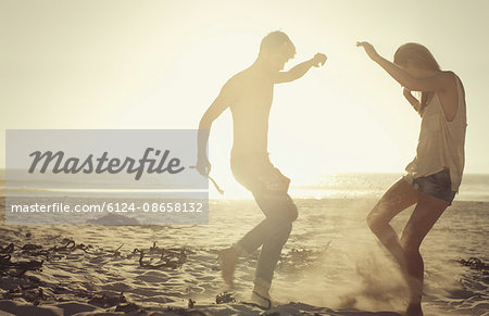 Playful couple dancing on sunny beach at sunset