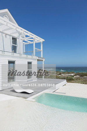 White beach house and swimming pool with ocean view under sunny blue sky