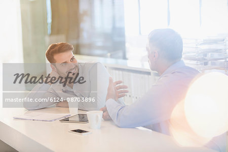 Businessmen with digital tablet and coffee talking in office