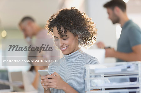 Smiling businesswoman texting with cell phone in office