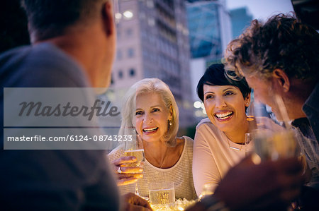 Smiling couples drinking white wine and talking at urban sidewalk cafe