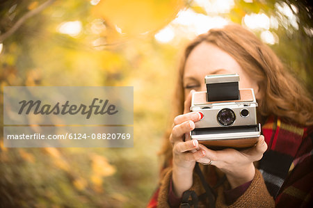 Portrait woman using old-fashioned instant camera in autumn woods