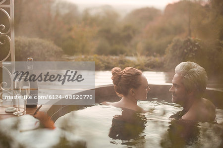 Couple talking soaking in hot tub with champagne on autumn patio