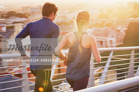 Runner couple running on sunny urban footbridge at sunrise Runner couple running on sunny urban footbridge at sunrise