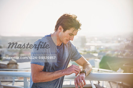 Sweaty male runner resting checking smart watch fitness tracker at sunny urban railing