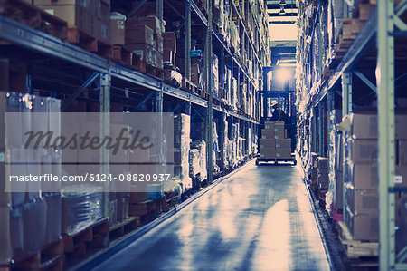 Worker operating forklift moving boxes along distribution warehouse shelves