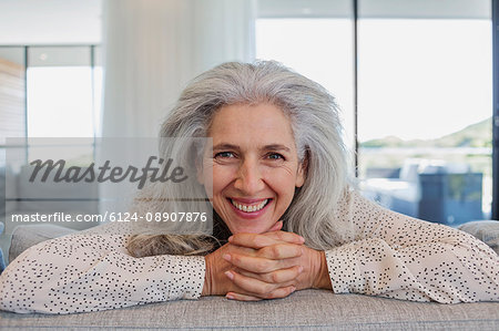Portrait happy mature woman leaning over sofa in living room