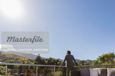 Businessman standing on balcony patio below sunny blue sky