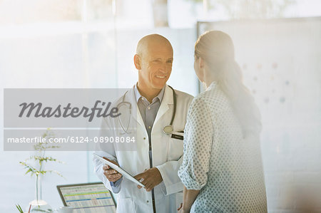Smiling male doctor showing digital tablet to female patient in doctor’s office Smiling male doctor showing digital tablet to female patient in doctor’s office