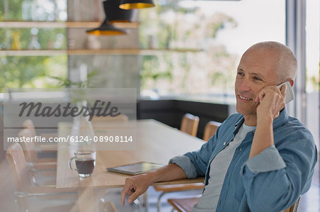 Smiling mature man talking on cell phone at dining table