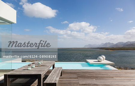 Sunny tranquil modern luxury patio with infinity pool and ocean view