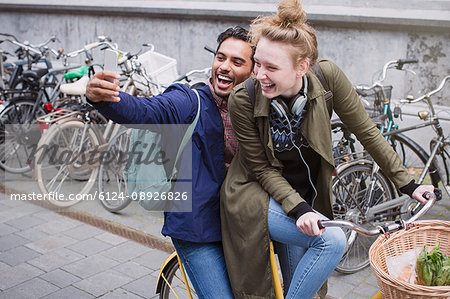 Playful, laughing young couple taking selfie with camera phone on bicycle Playful, laughing young couple taking selfie with camera phone on bicycle