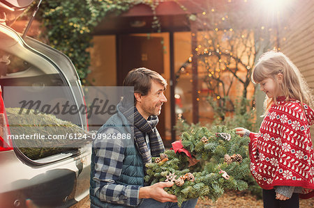 Father and daughter with Christmas wreath outside car