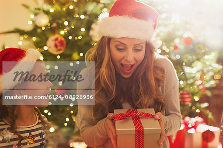 Surprised mother with Santa hat receiving Christmas gift from daughter Surprised mother with Santa hat receiving Christmas gift from daughter
