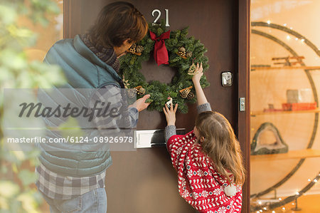 Father And Daughter Hanging Christmas Wreath On Front Door