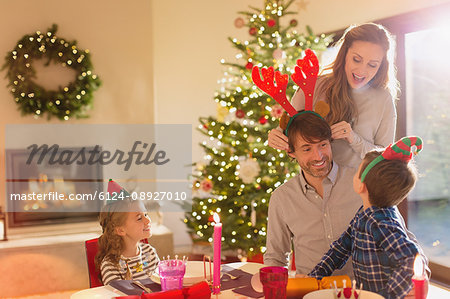 Family wearing elf and costume reindeer antlers at Christmas dining table