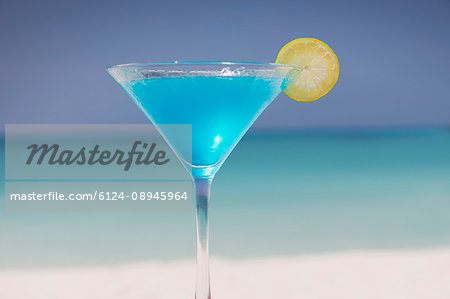 Blue cocktail with lemon slice in martini glass on tropical ocean beach