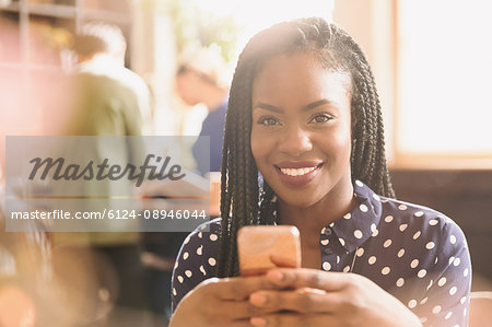 Portrait smiling African woman texting with cell phone in cafe