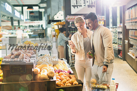 Young couple with cell phone grocery shopping at market