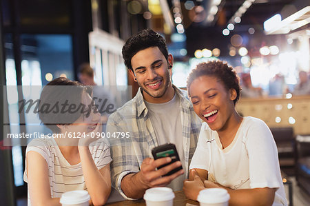 Young friends using cell phone, texting and laughing at cafe