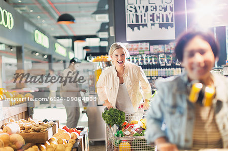 Playful young woman laughing, pushing shopping cart in grocery store market