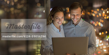 Smiling businessman and businesswoman working late at laptop in office at night