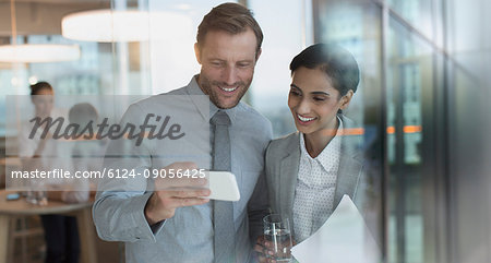 Smiling businessman and businesswoman watching video on smart phone in office Smiling businessman and businesswoman watching video on smart phone in office