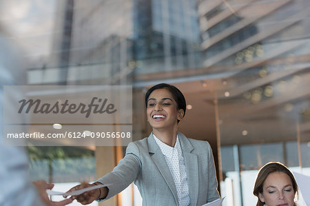Smiling businesswoman handing paperwork to colleague in conference room meeting