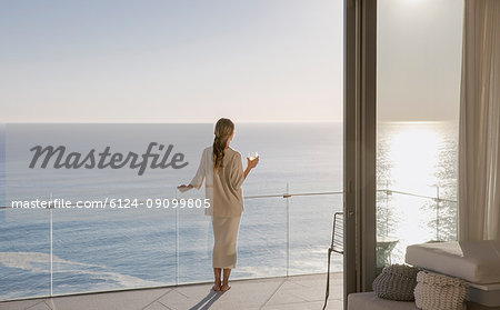 Woman standing on sunny luxury balcony with ocean view