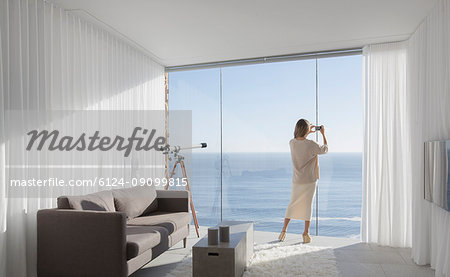 Woman with camera phone photographing sunny ocean view from modern, luxury home showcase interior living room