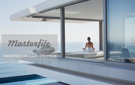 Serene woman meditating on modern, luxury home showcase exterior patio with ocean view