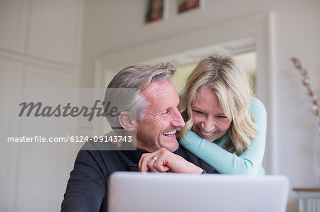 Laughing, carefree mature couple using laptop