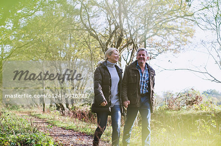 Happy mature couple holding hands, walking in autumn park