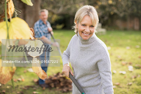 Portrait smiling, confident mature woman raking leaves in autumn backyard