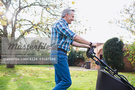 Senior man moving lawn with lawnmower in autumn backyard