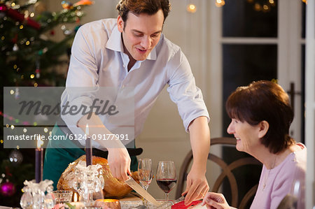 Son serving Christmas turkey to senior mother at candlelight dinner table