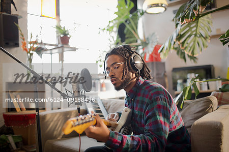 Young male musician recording music, playing guitar at microphone in apartment