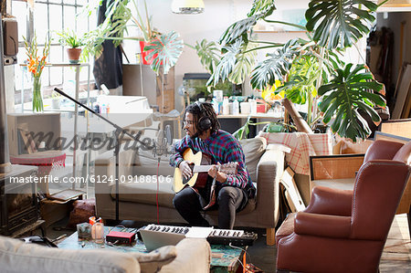 Young male musician recording music, playing guitar and singing into microphone in apartment