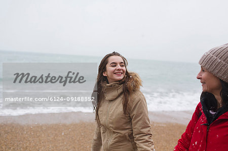 Mother and daughter in warm clothing walking on winter ocean beach