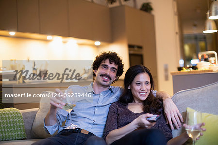 Happy couple drinking white wine and watching TV on apartment sofa