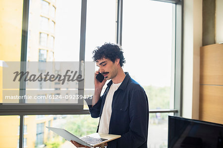 Man using laptop and talking on smart phone at urban apartment window