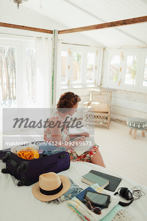 Woman writing in journal next to suitcase in beach hut bedroom